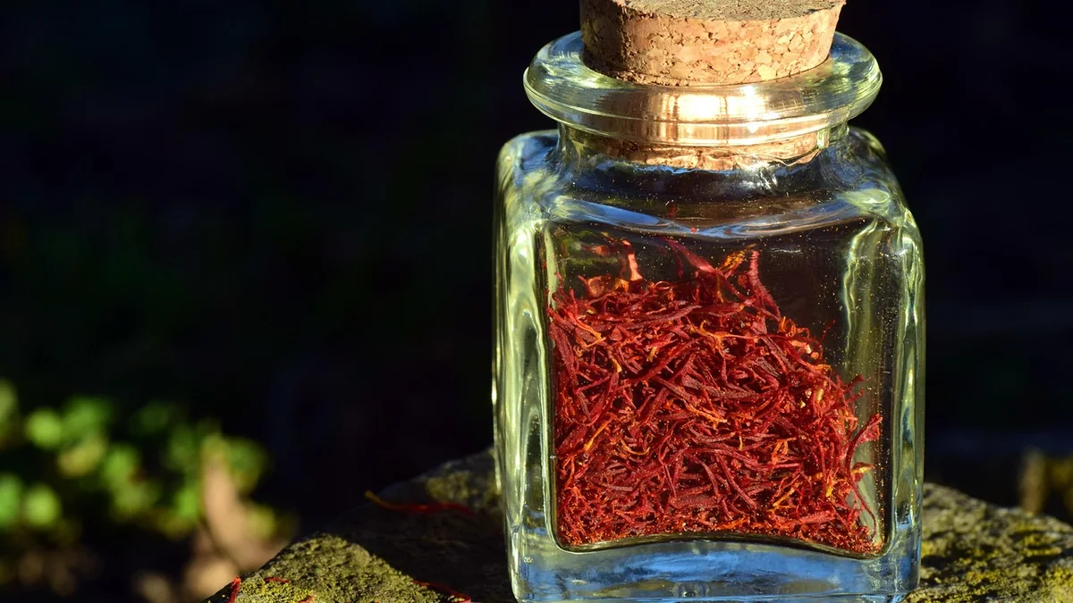 A glass jar filled with deep red saffron threads resting on stone against a dark background.