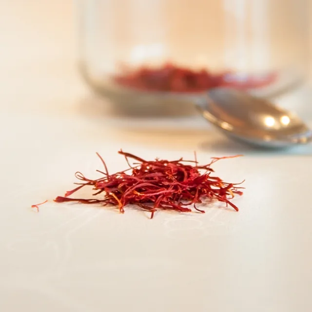 A small measured pinch of saffron threads on a pale surface beside a softly blurred spoon and jar.